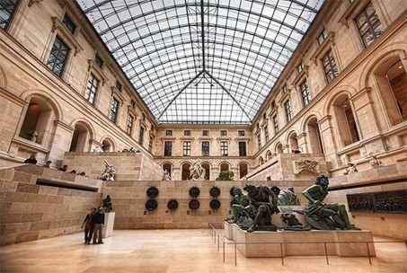 C'est l'intérieur du musée du louvres. On voit sur notre droite un statue avec plusieurs hommes en vert et en haut des fenêtres. on peut voir le ciel.