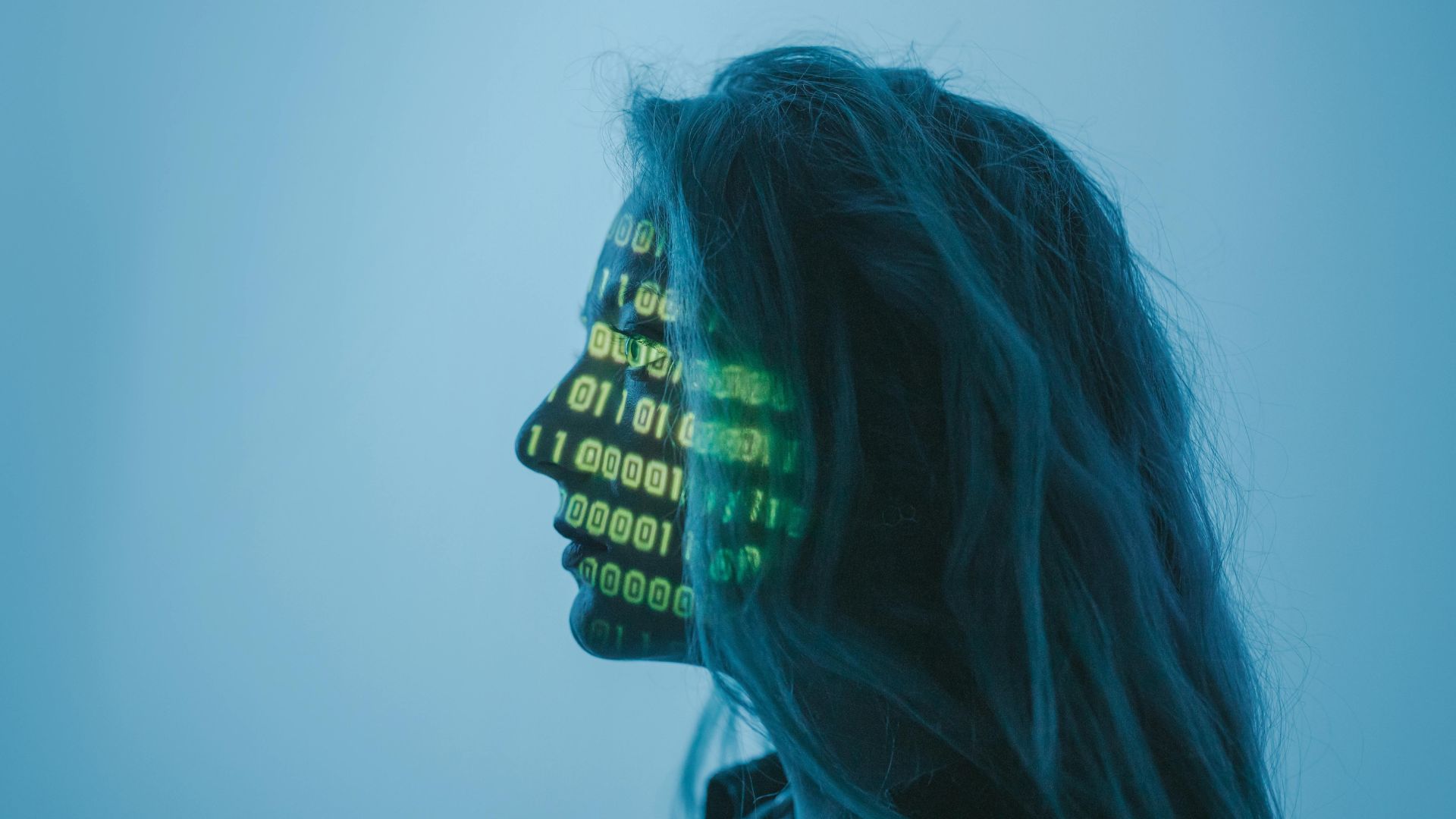 On peut voir le visage d'une femme de profil avec un fond bleu. Sur son visage il y a les chiffres binaires informatiques 0 et 1 qui sont inscrits en vert.